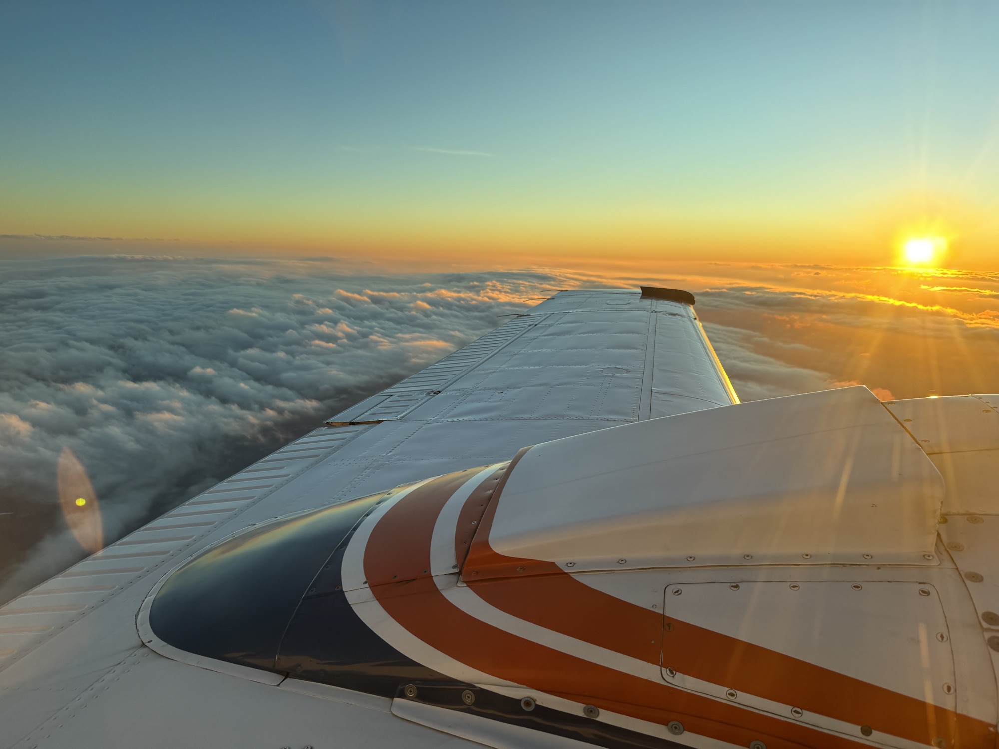 View over the wing of a Beechcraft Baron 58 at sunset above the clouds